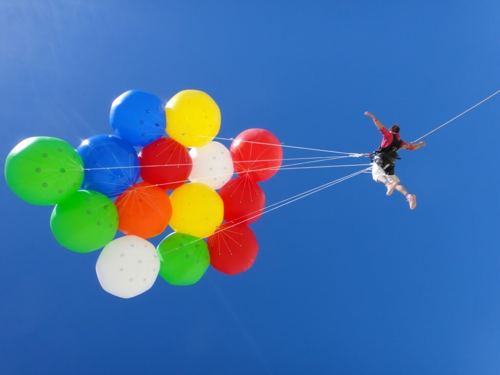 A man flying on colorful weather balloons with arms outstretched.