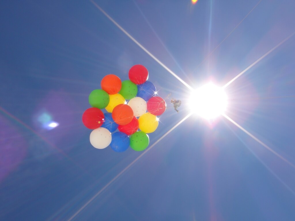 A person riding colorful weather balloons with the sun and vibrant blue sky in the background.